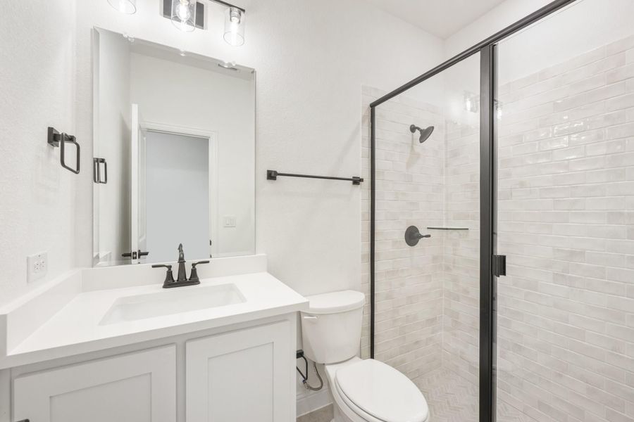 Bathroom with white vanity, toilet, and glass-enclosed tile shower with black fixtures