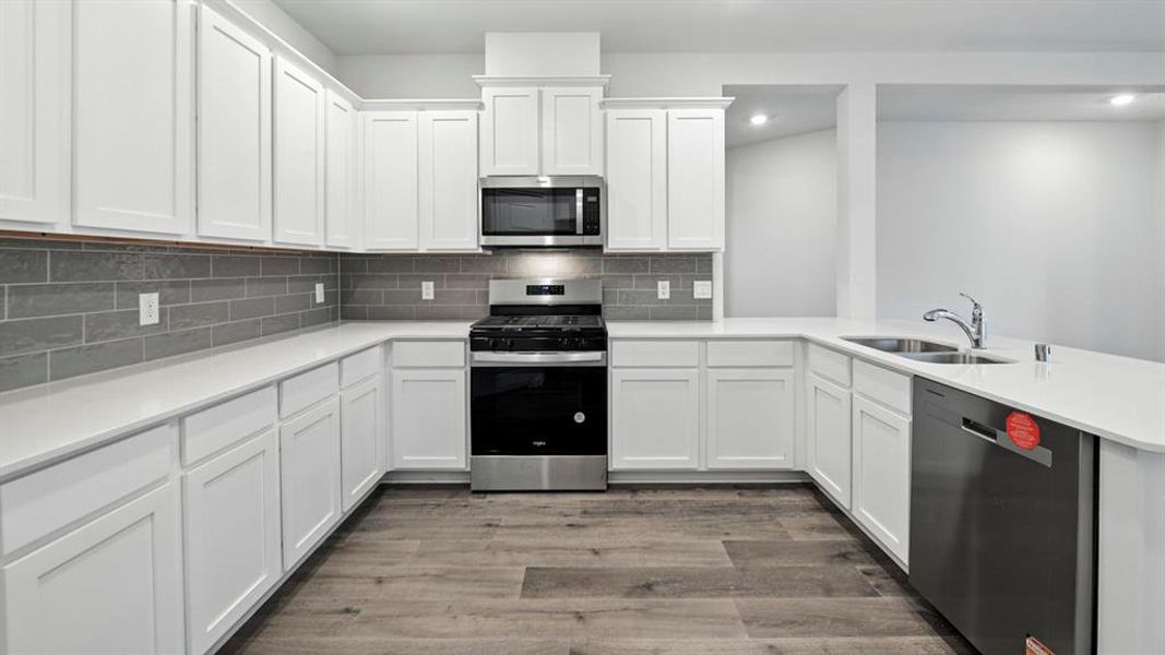 Kitchen featuring stainless steel appliances, white cabinets, decorative backsplash, light wood-style floors, and light stone countertops Kitchen featuring stainless steel appliances, white cabinets, decorative backsplash, light wood-style floors, and light stone countertops