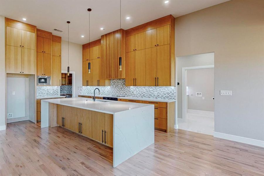 Kitchen with tasteful backsplash, stainless steel microwave, a kitchen island with sink, light hardwood / wood-style flooring, and sink