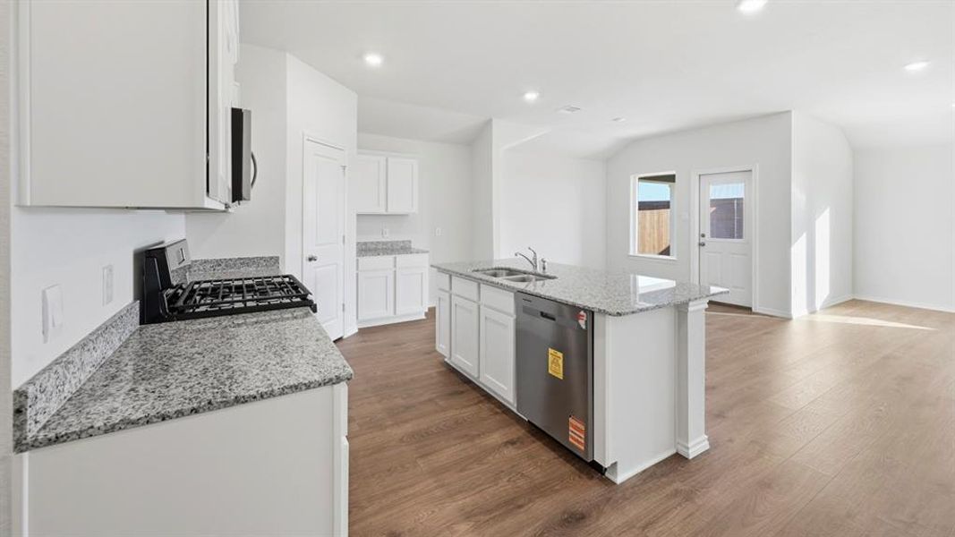 Kitchen with light stone counters, stainless steel appliances, a kitchen island with sink, white cabinets, and dark wood-style floors