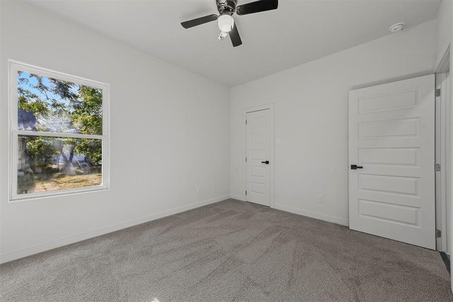 Unfurnished bedroom featuring a raised ceiling, light carpet, ensuite bath, and ceiling fan