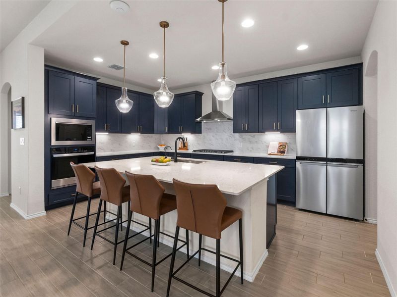 Kitchen featuring arched walkways, a kitchen bar, stainless steel appliances, an island with sink, and light stone countertops