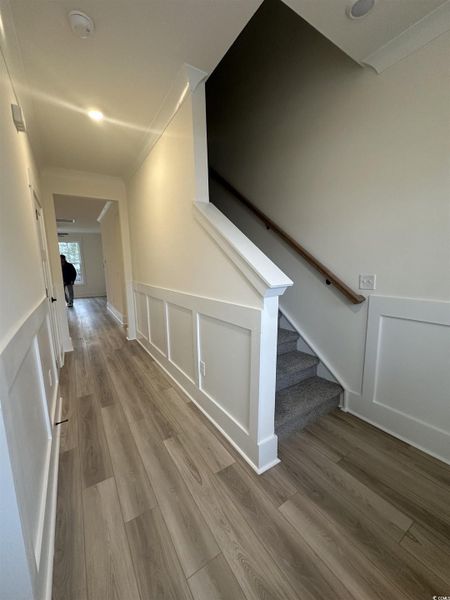 Corridor with light wood finished floors, stairs, a decorative wall, and wainscoting