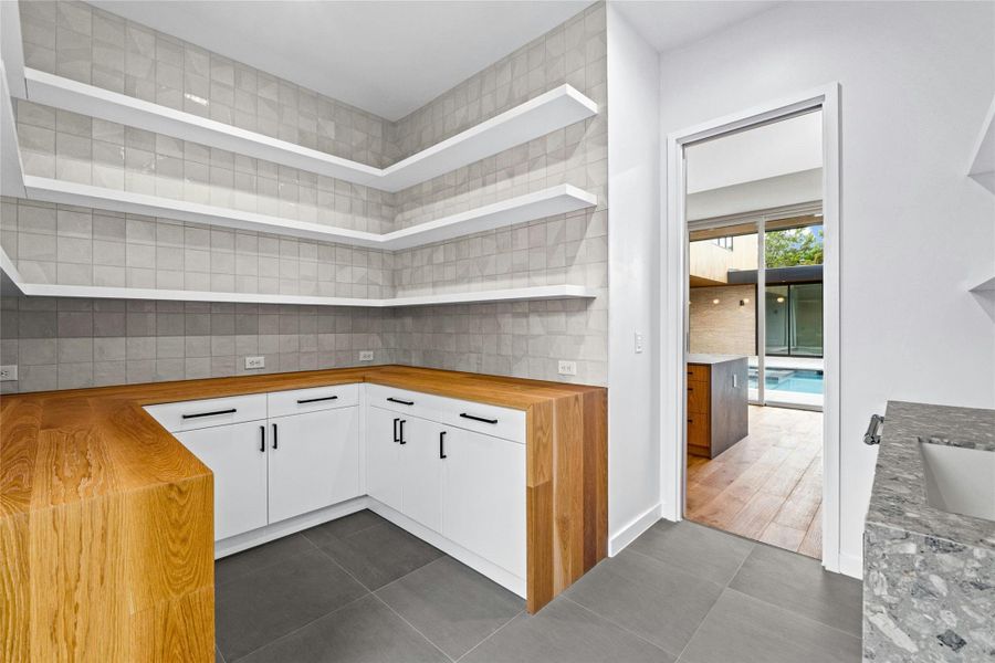 Butler's pantry/prep kitchen conveniently located off the main kitchen. Notice plentiful shelving. Flooring is 24"x24" Refin Ceramics Wide Steel and tiles are 55.5 Cas Blanco 2.0 Wiind Hatch.