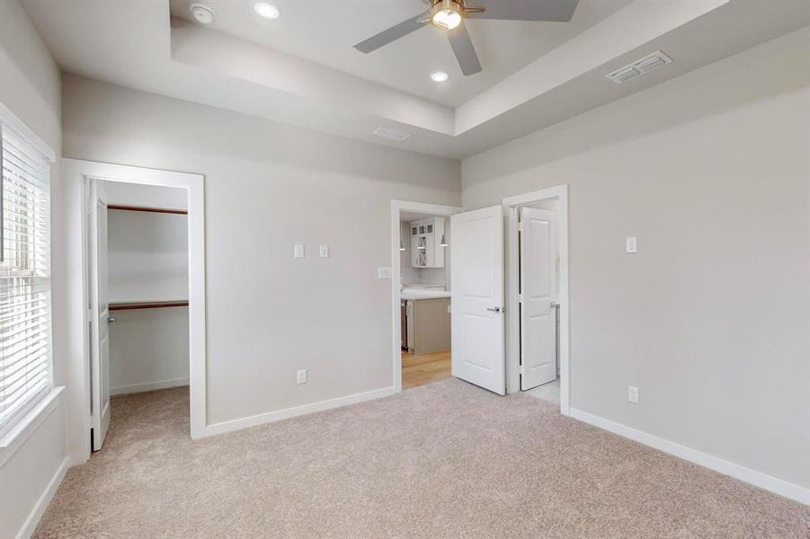 Unfurnished bedroom with a raised ceiling, ceiling fan, a spacious closet, light colored carpet, and a closet