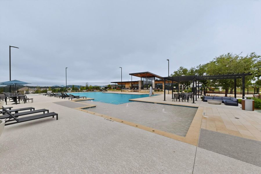 Expansive outdoor pool area featuring a large swimming pool, an integrated shallow water feature with fountains, and an adjacent modern clubhouse building