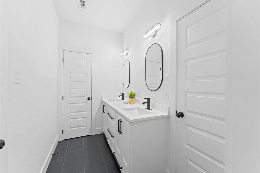 The dual-sink vanity rests below modern lighting and stylish mirrors.
