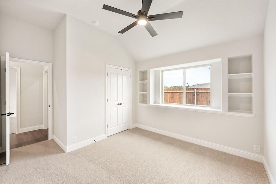 Empty bedroom with vaulted ceiling, ceiling fan, built-in shelves, and carpet flooring