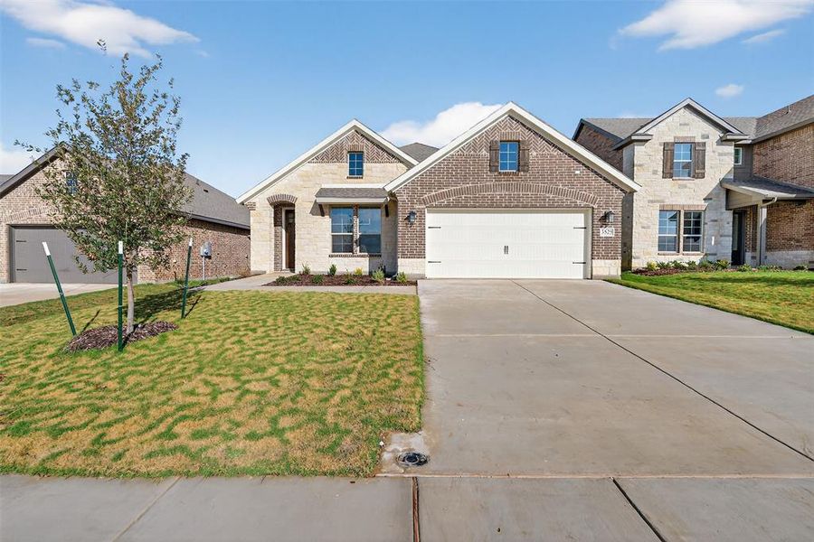 View of front facade with brick siding, a front lawn, driveway, and stone siding