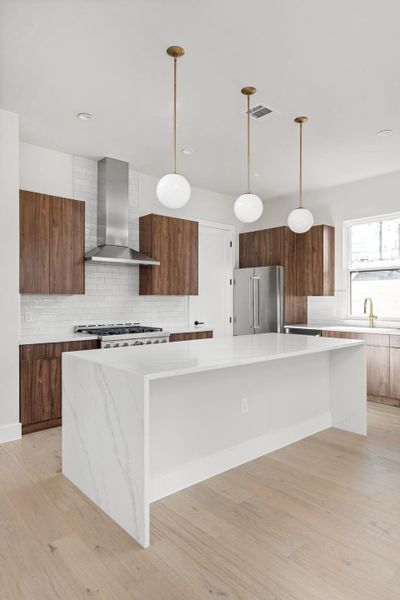 Kitchen featuring modern cabinets, a spacious island, high quality fridge, wall chimney exhaust hood, and cooktop