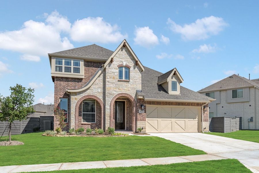 Two-story home with brick and stone exterior, arched entryway, two-car garage, and green front lawn.