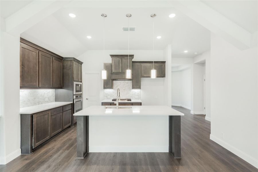 Kitchen with large white island, dark wood cabinets, pendant lights, and hardwood floors under vaulted ceiling Kitchen with large white island, dark wood cabinets, pendant lights, and hardwood floors under vaulted ceiling