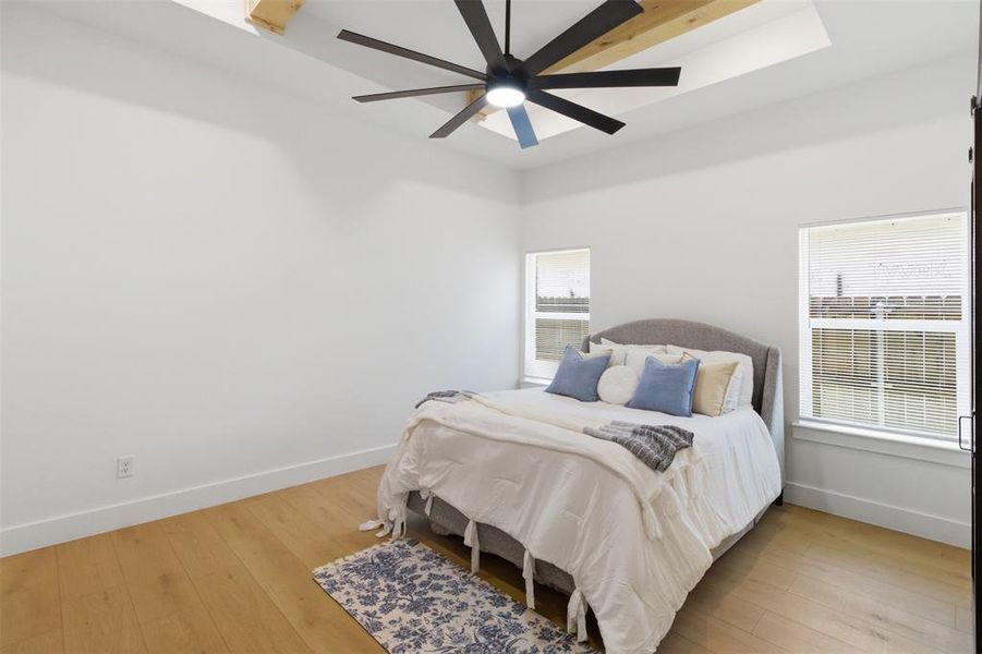 Room featuring a tray ceiling with exposed wood beams, a contemporary ceiling fan, wood-finish flooring, and multiple windows