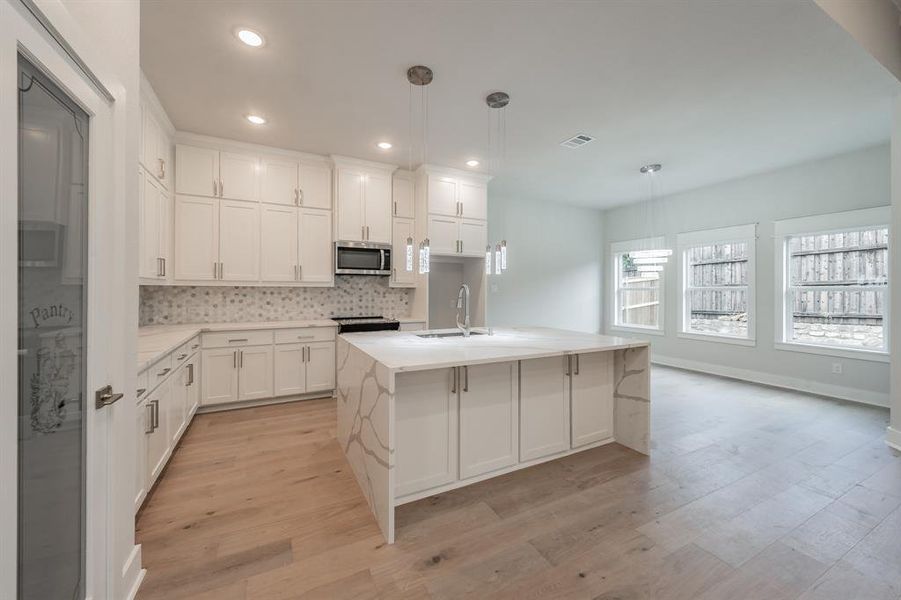 Kitchen with recessed lighting, tasteful backsplash, white cabinetry, light stone counters, and an island with sink