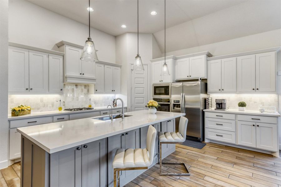 Kitchen with white cabinets, stainless steel appliances, light wood-style flooring, and vaulted ceiling