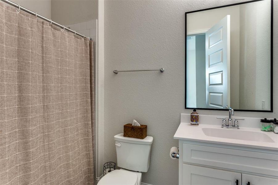 Full bathroom with a textured wall, vanity, and a shower with shower curtain Full bathroom with a textured wall, vanity, and a shower with shower curtain