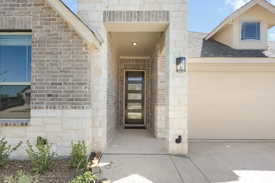 Covered front entry with brick and stone exterior, modern door with glass panels, and attached garage nearby.