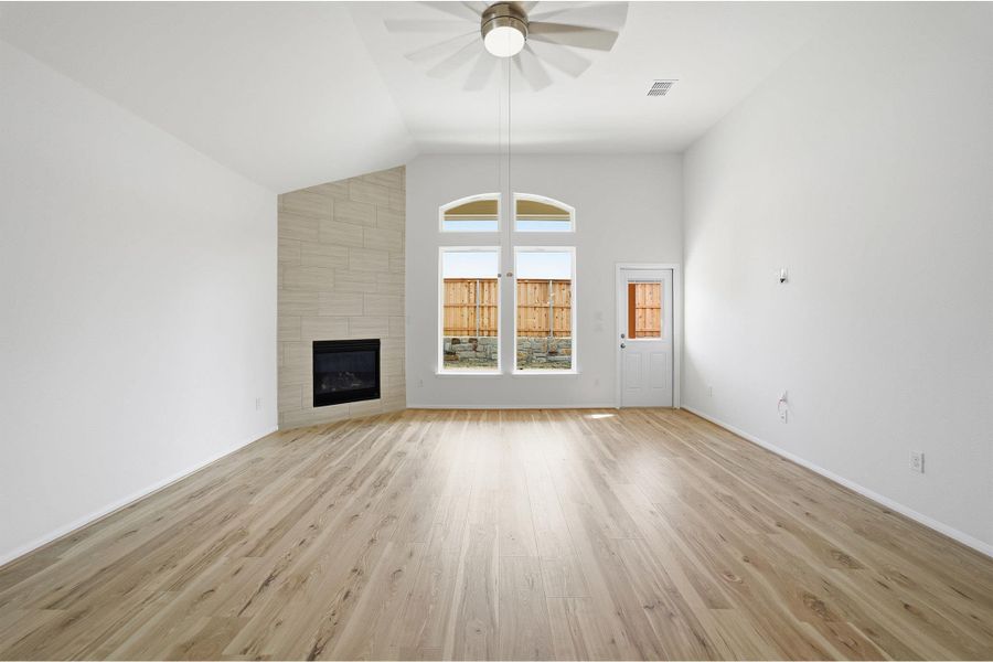 Unfurnished living room with light wood-style flooring, a tiled fireplace, ceiling fan, and lofted ceiling