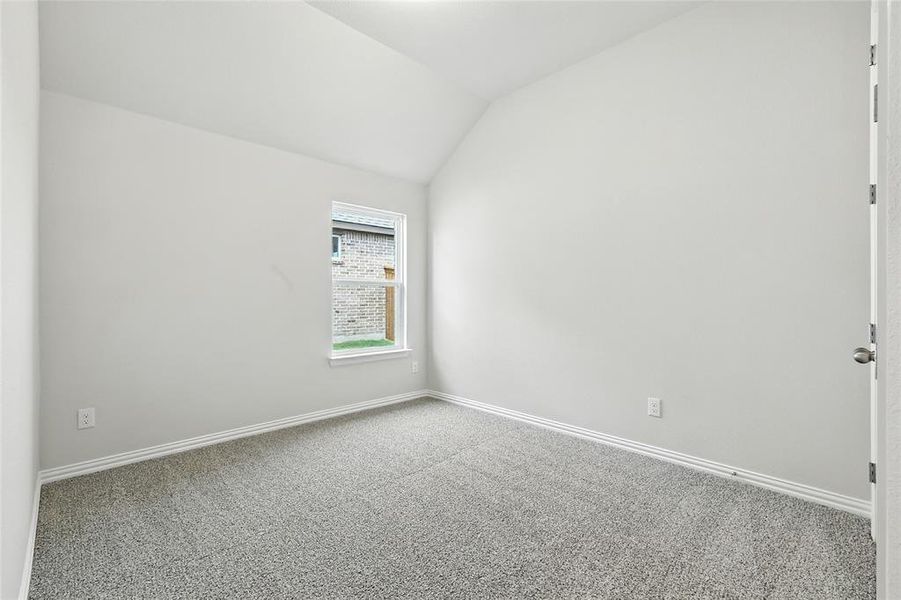 Carpeted spare room featuring baseboards and vaulted ceiling