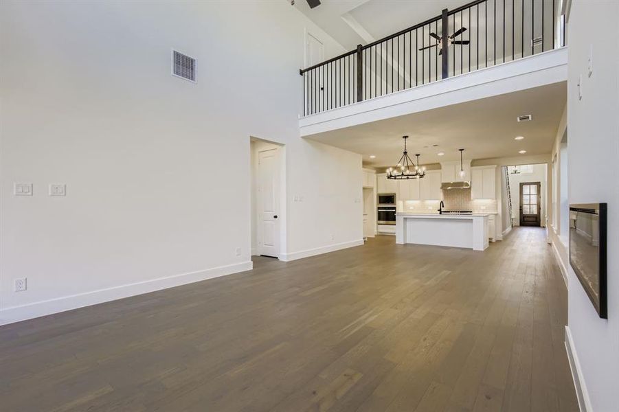 Unfurnished living room with dark wood-style floors, a chandelier, a high ceiling, a ceiling fan, and a glass covered fireplace Unfurnished living room with dark wood-style floors, a chandelier, a high ceiling, a ceiling fan, and a glass covered fireplace