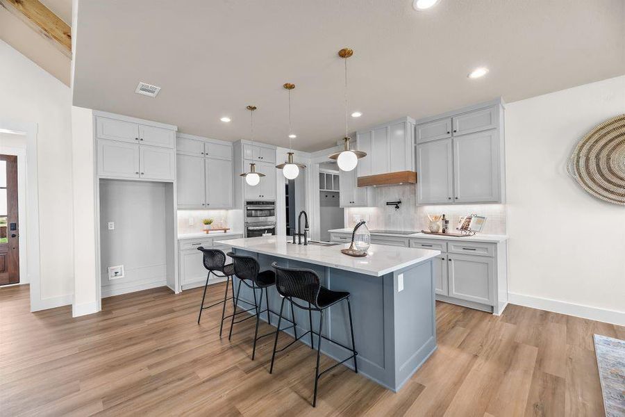 Kitchen featuring pendant lighting, a breakfast bar, gray cabinets, backsplash, and a center island with sink Kitchen featuring pendant lighting, a breakfast bar, gray cabinets, backsplash, and a center island with sink