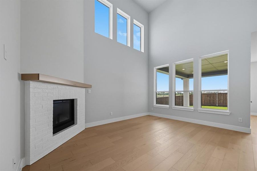 Unfurnished living room with a fireplace, light wood-style flooring, and a towering ceiling