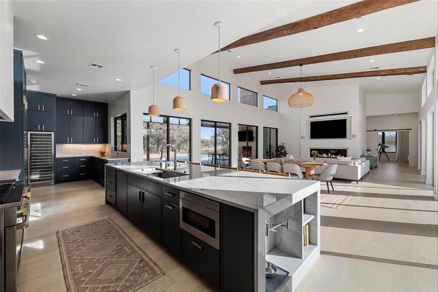 Kitchen with dark cabinets, hanging light fixtures, a large island with sink, backsplash, and wine cooler
