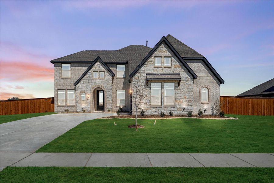 Two-story stone and brick home with arched entry, large windows, and manicured front lawn at dusk Two-story stone and brick home with arched entry, large windows, and manicured front lawn at dusk