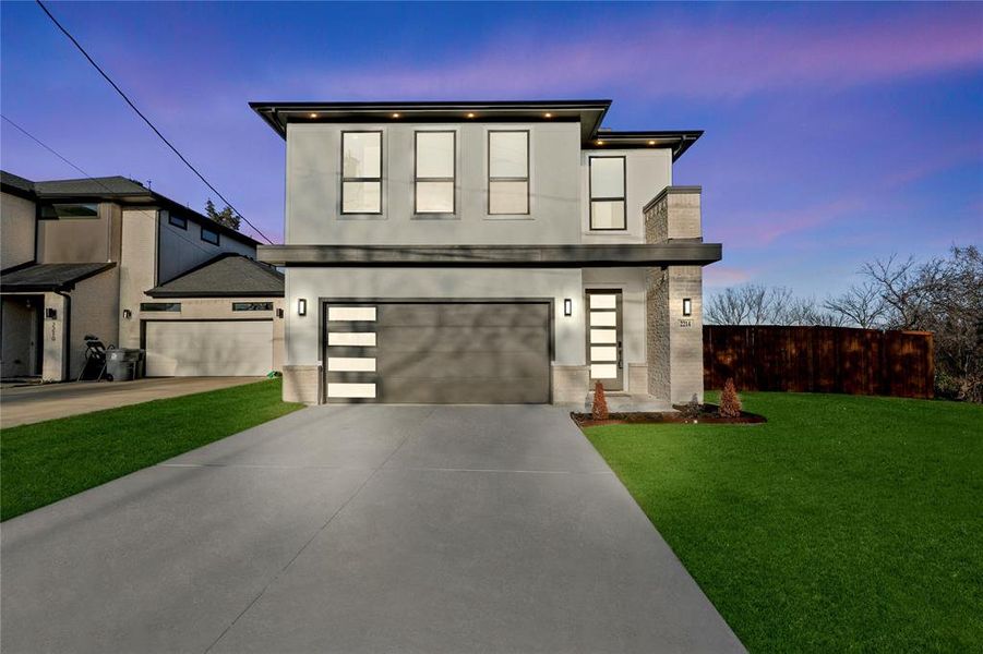 Contemporary home with concrete driveway, a lawn, fence, and a garage