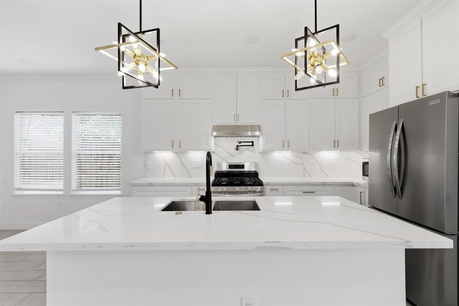 Chef's kitchen island with white quartz countertops, designer pendant lights, and stainless steel appliances.