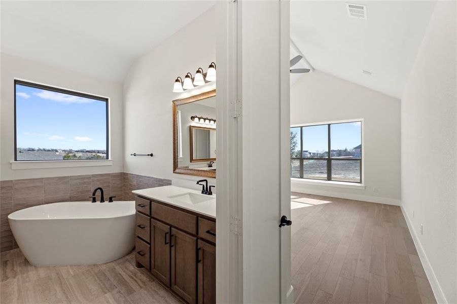 Bathroom with hardwood / wood-style floors, vaulted ceiling, a bathing tub, and a water view