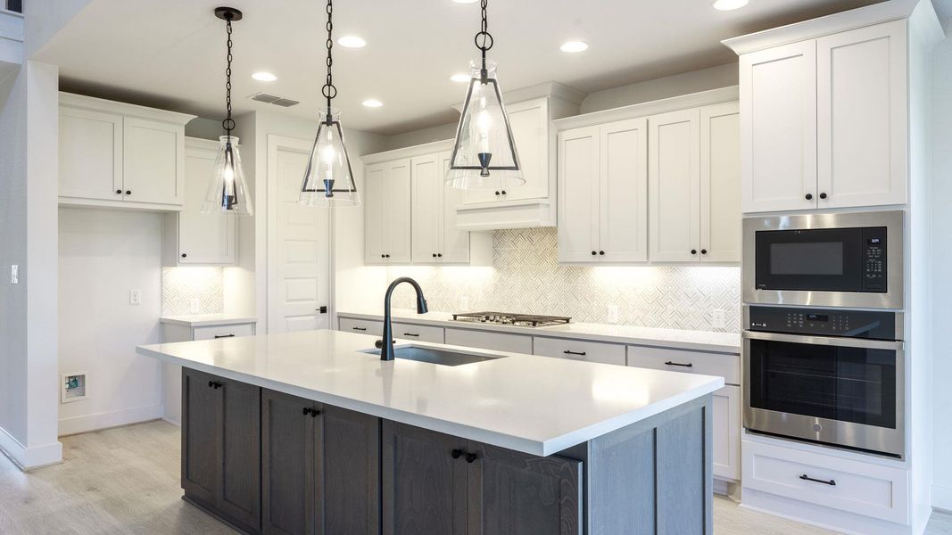 Kitchen featuring backsplash, appliances with stainless steel finishes, white cabinetry, light wood finished floors, and a center island with sink Kitchen featuring backsplash, appliances with stainless steel finishes, white cabinetry, light wood finished floors, and a center island with sink