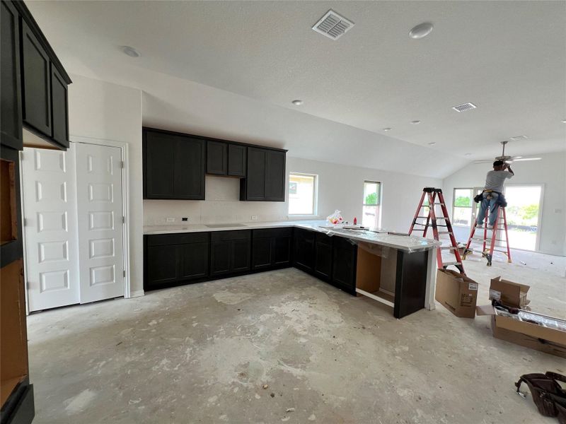 Kitchen with lofted ceiling, unfinished concrete floors, a peninsula, dark cabinets, and light countertops