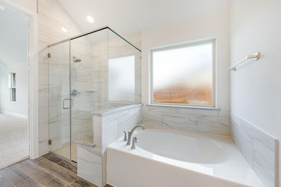 Master bathroom with soaking tub, glass-enclosed shower, marble tile walls, and frosted window