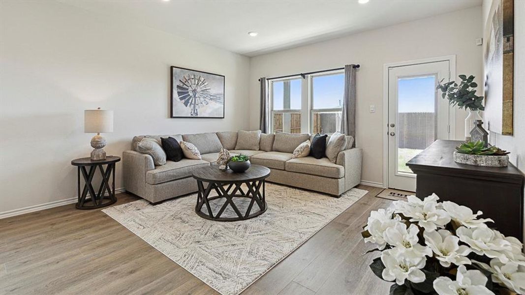 Living room featuring light-toned flooring, large windows with curtains, and a door leading to the exterior