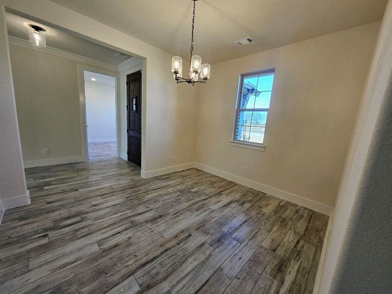 Empty room featuring a chandelier, wood finished floors, and ornamental molding