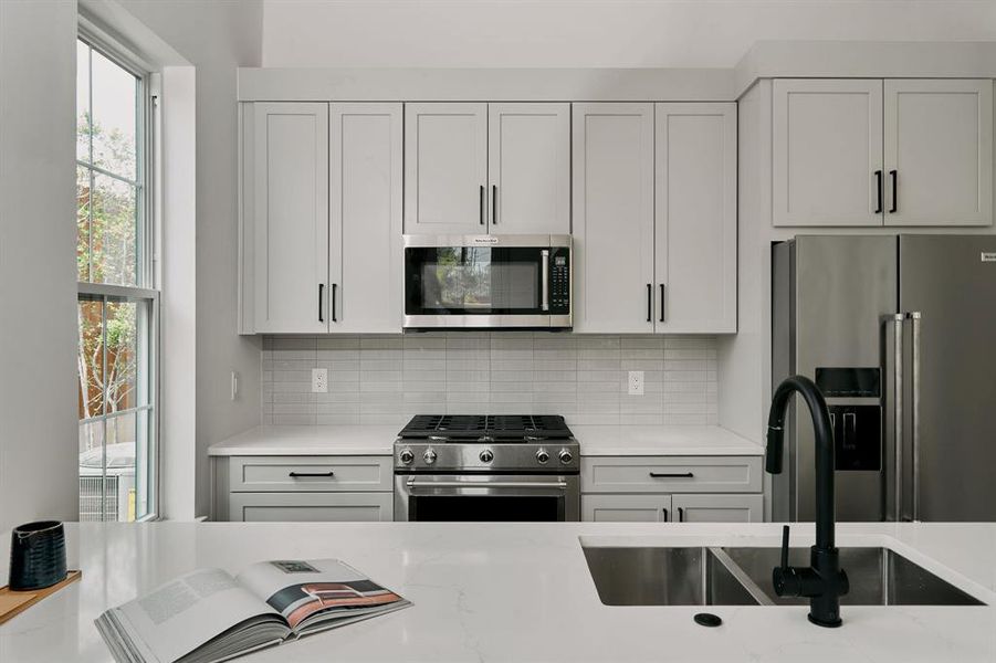 Modern kitchen featuring light gray shaker cabinetry, stainless steel appliances, a white subway tile backsplash, and light-toned countertops