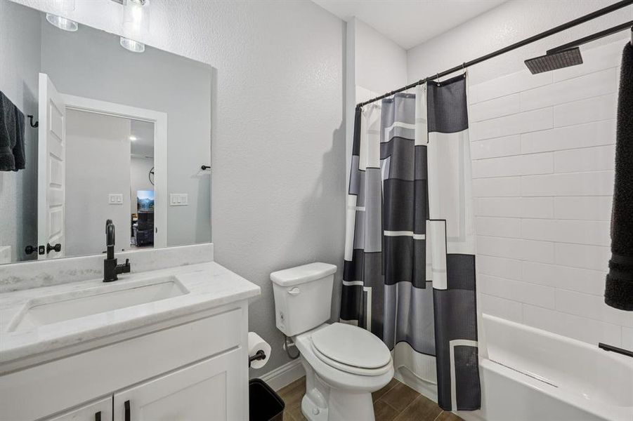 Full bath with shower / bath combo, vanity, a textured wall, and wood tiled floors Full bath with shower / bath combo, vanity, a textured wall, and wood tiled floors