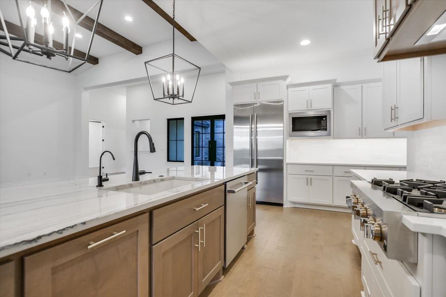 Kitchen with built in appliances, a chandelier, light wood finished floors, beam ceiling, and light stone countertops