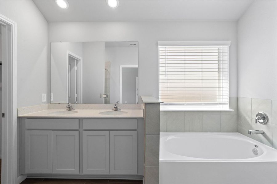 A bright and functional primary bath offering dual sinks for busy mornings, a large mirror, soaking tub, and a modern glass-enclosed shower, creating a serene and efficient space.