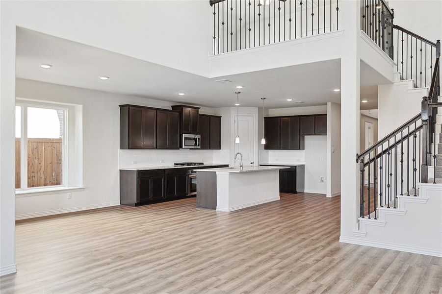 Kitchen featuring a center island with sink, light hardwood / wood-style floors, hanging light fixtures, sink, and a towering ceiling