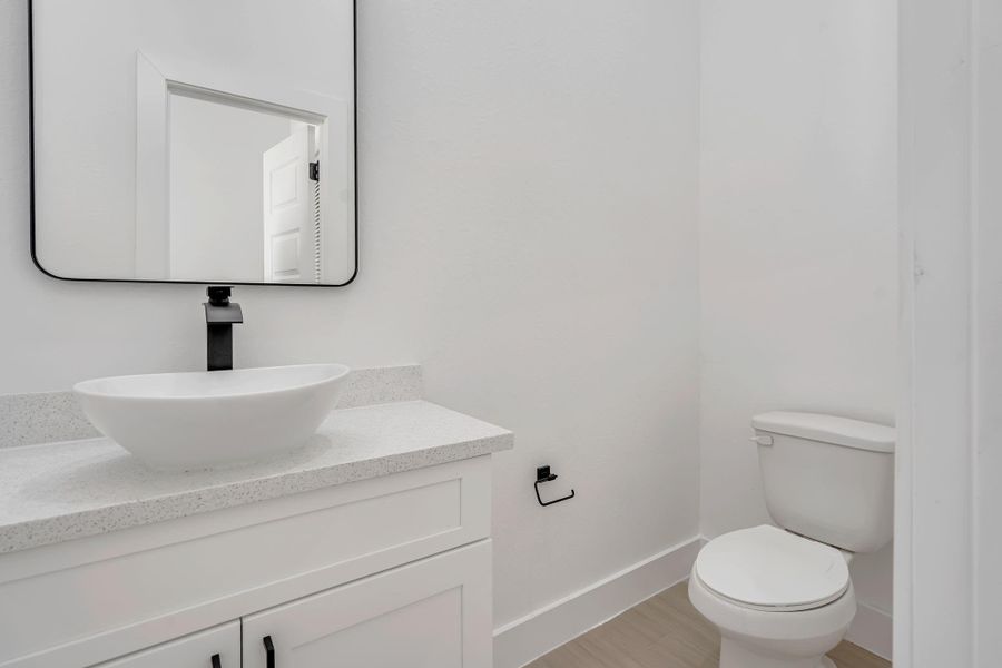 Convenient first-floor half bath featuring a modern vessel sink, quartz countertop vanity, and sleek black fixtures that complement the home’s contemporary design.