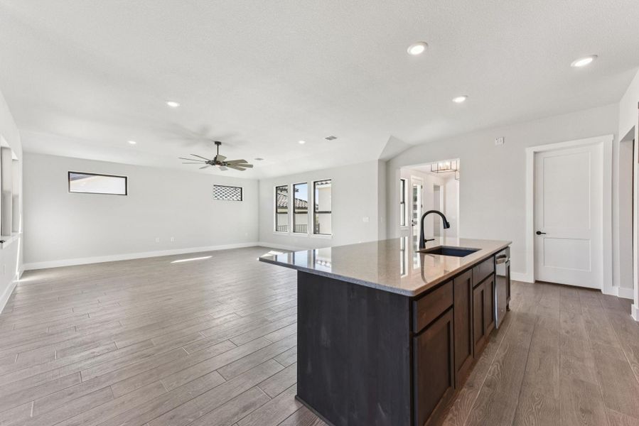 Kitchen with light stone counters, an island with sink, recessed lighting, dark brown cabinets, and open floor plan Kitchen with light stone counters, an island with sink, recessed lighting, dark brown cabinets, and open floor plan