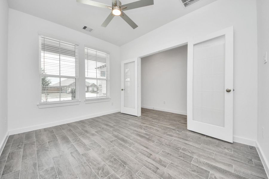 Experience the perfect blend of sophistication and warmth in this home office, boasting elegant wood-look tile flooring and flooded with natural light from expansive windows and French doors. Sample photo of completed home with similar floor plan. Actual colors and selections may vary.