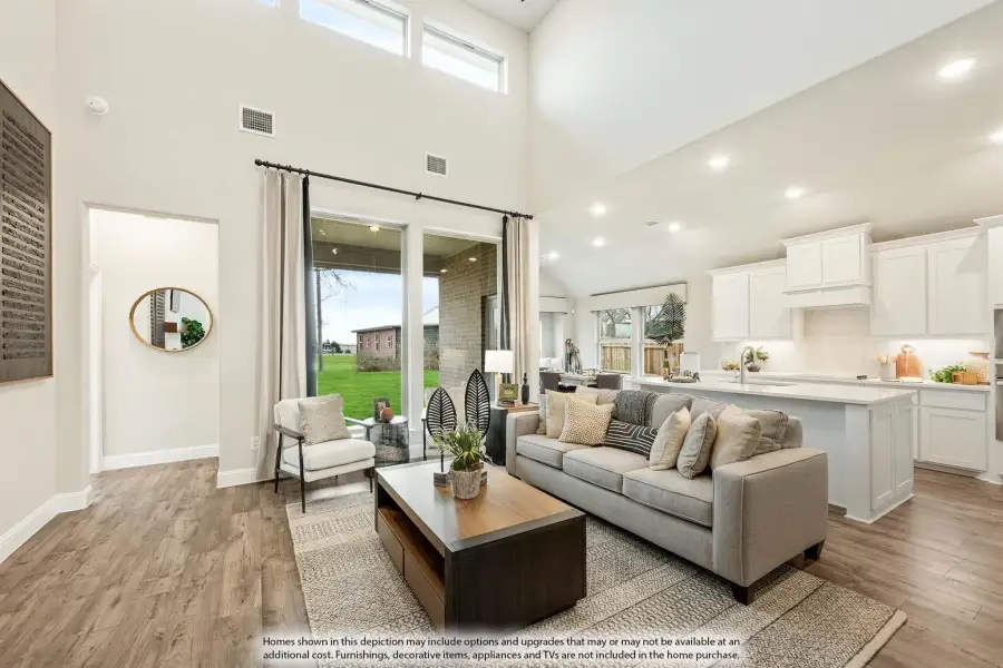 Open-concept living room with two-story ceiling, hardwood floors, and kitchen visible in background