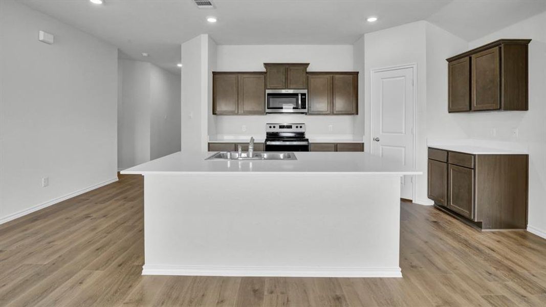 Kitchen with a center island with sink, stainless steel appliances, recessed lighting, dark wood finish cabinetry, and light wood-type flooring