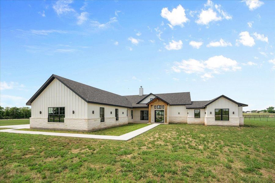 Back of property with board and batten siding, stone siding, a lawn, and a shingled roof
