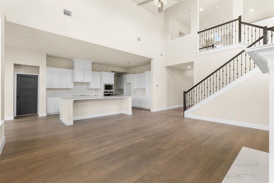 Unfurnished living room featuring dark hardwood / wood-style floors, ceiling fan, and a towering ceiling