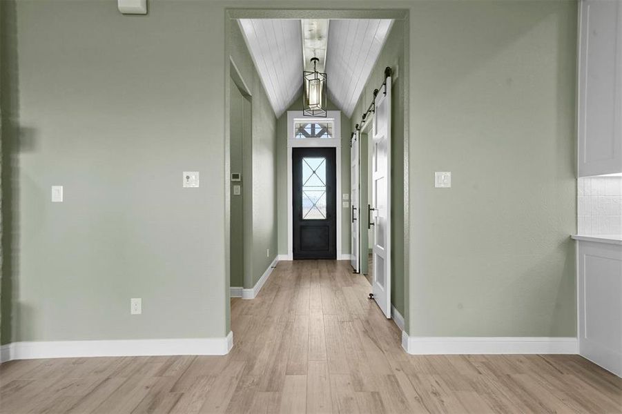 Entryway featuring a barn door, light hardwood / wood-style flooring, vaulted ceiling, and wood ceiling