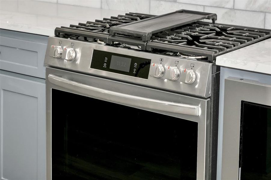 Detailed view of stainless steel range with gas cooktop, decorative backsplash, and light countertops Detailed view of stainless steel range with gas cooktop, decorative backsplash, and light countertops